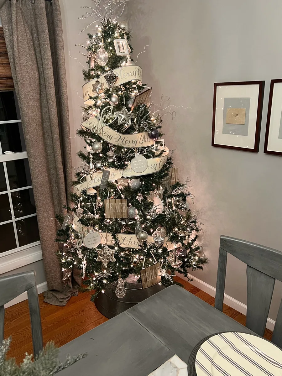 A silver and cream Christmas tree with graceful ribbon and snowflake topper.