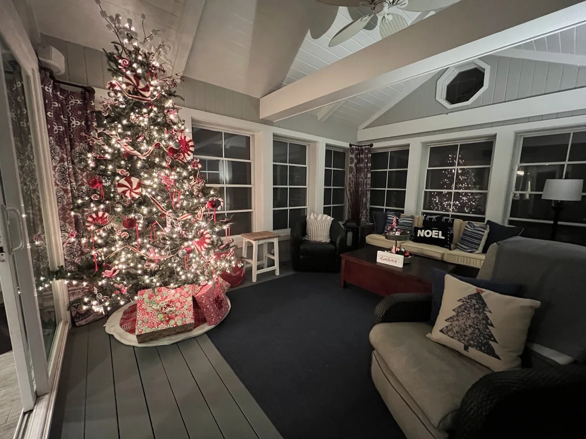 A candy-cane themed Christmas tree completes a cheerful enclosed porch.