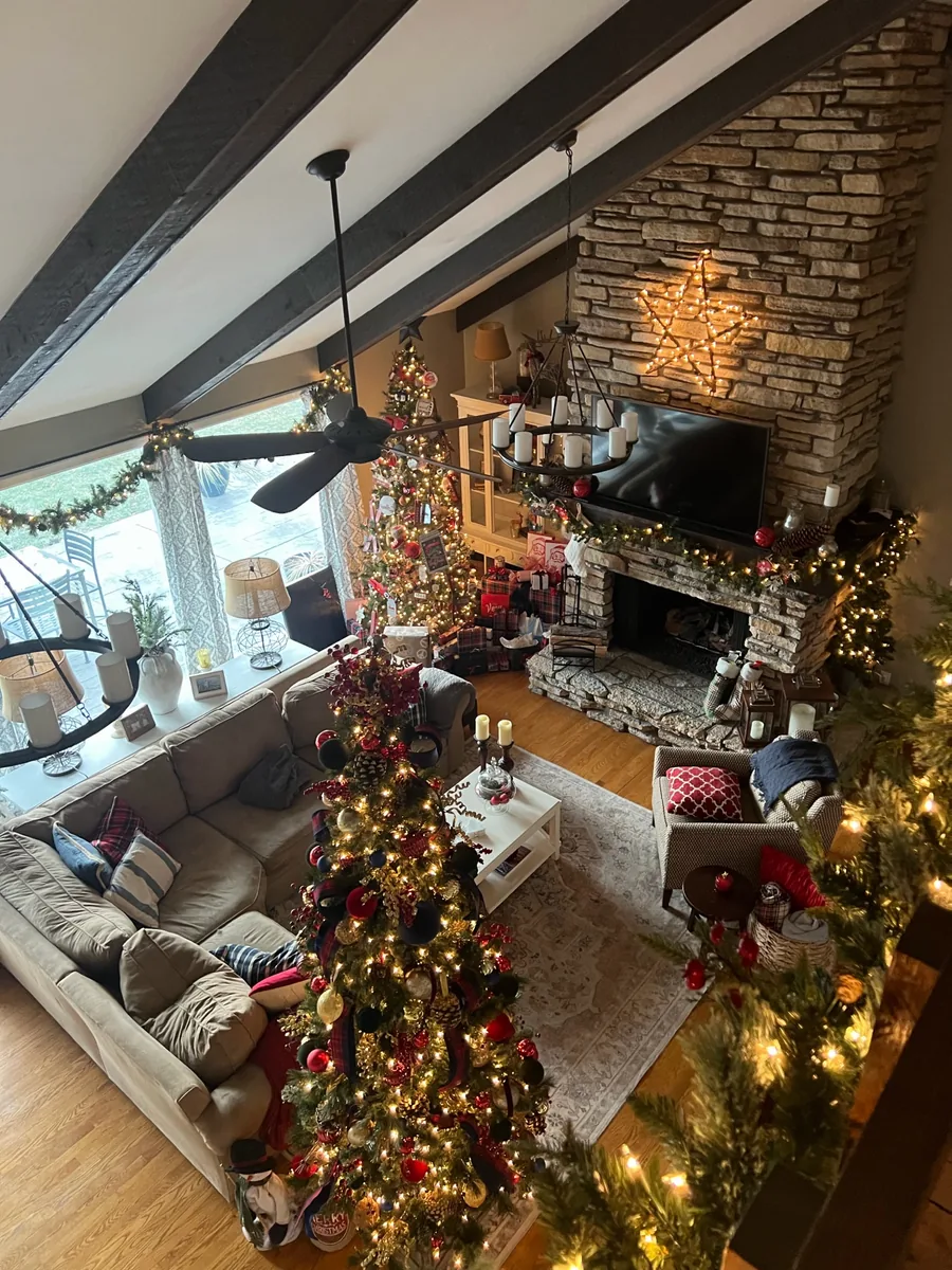A warmly lit holiday living room with multiple decorated Christmas trees and garlands.
