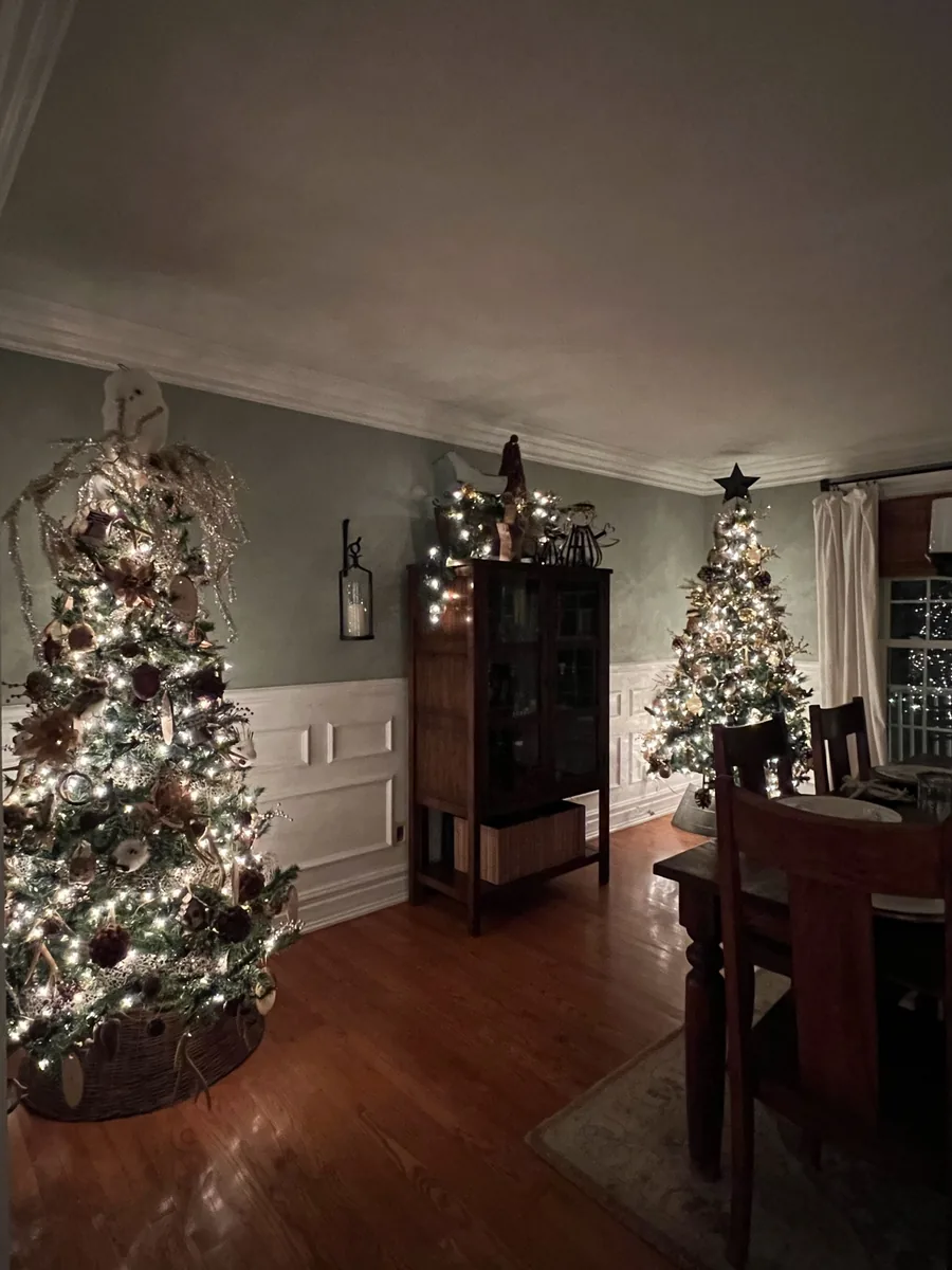 Two decorated Christmas trees bring soft light and natural textures to a dining room.